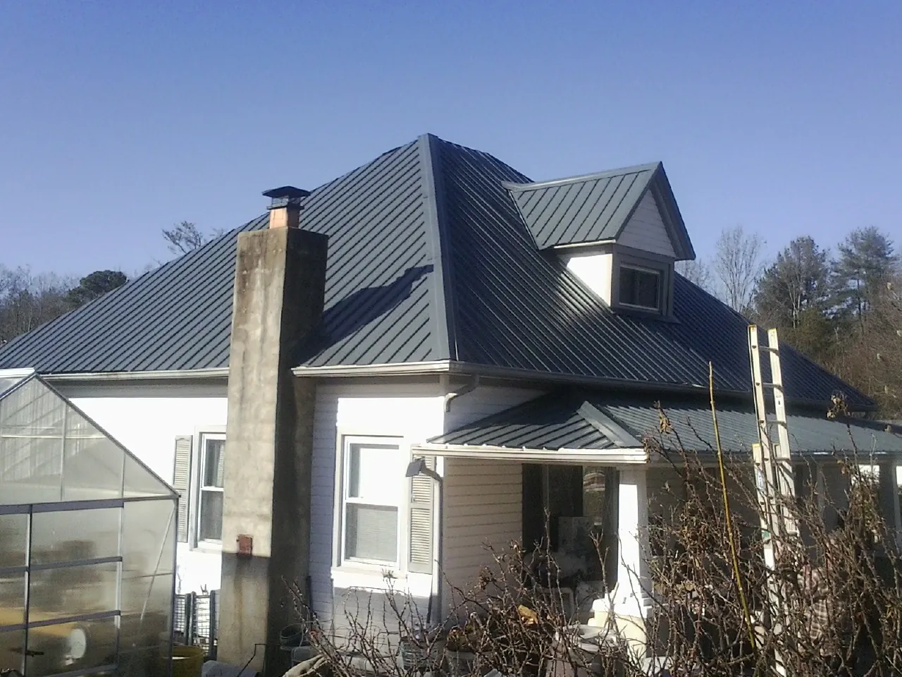Dark blue standing seam metal roof on a white farmhouse with dormer — Slate & Tile Roof Repair by Roofing Brothers in Hillister