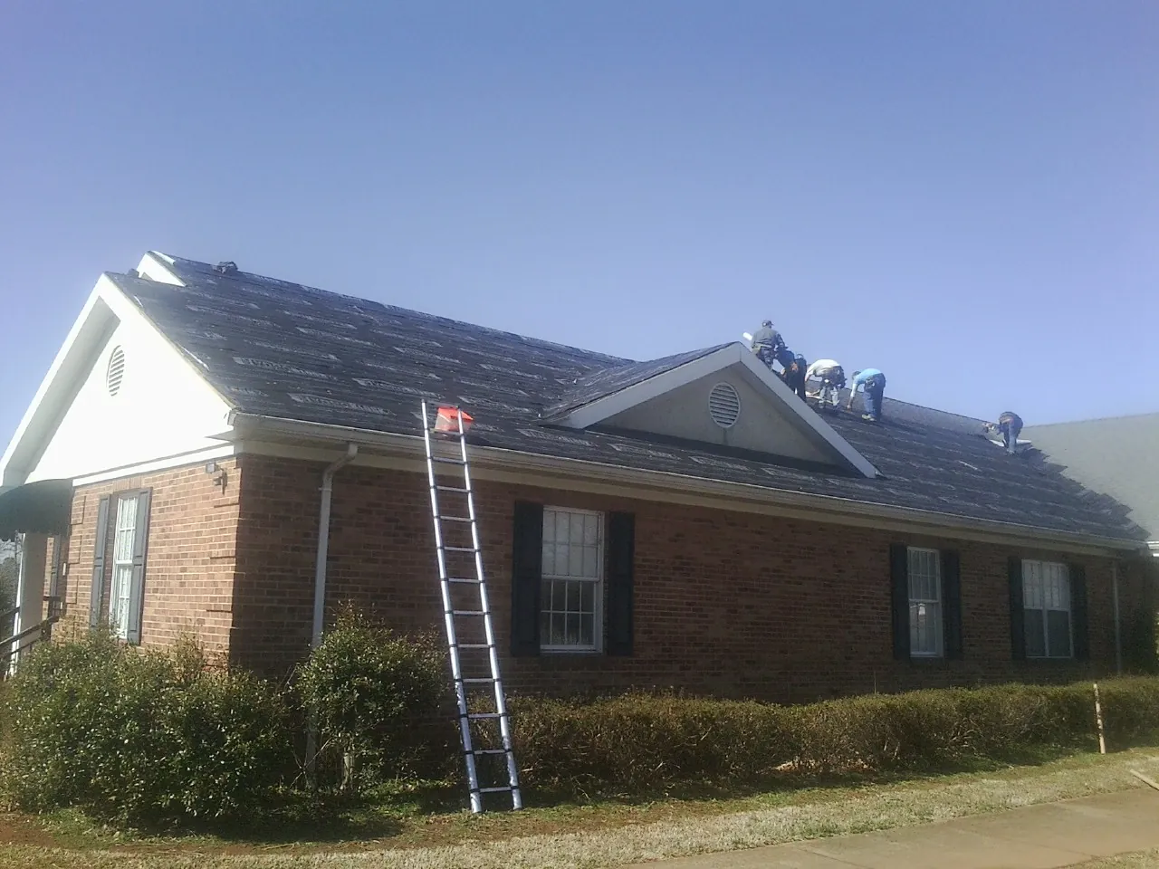 Crew tearing shingles off a brick ranch roof with a ladder set — Emergency Roof Repair work by our crew in Hillister