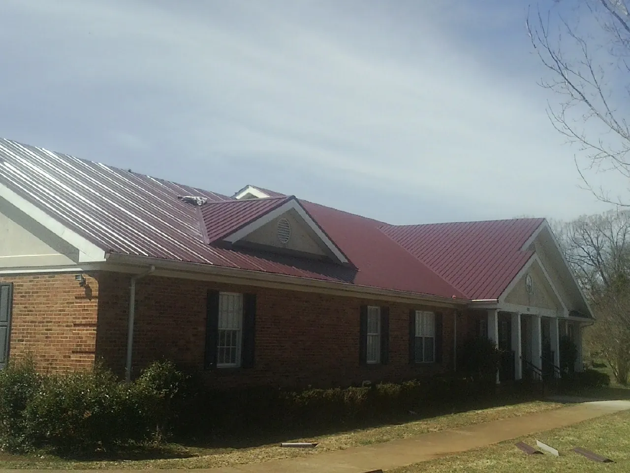 Red metal roof with gabled entries on a long brick building, from a Hail Damage Roof Repair job in Hillister