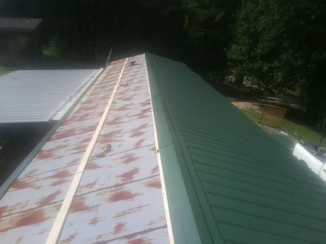 Old rusted panels beside newly installed green metal roofing — Wind Damage Roof Repair by Roofing Brothers in Hillister