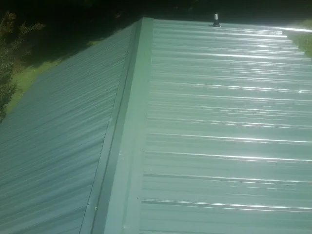 New green metal panels meeting at the ridge of a roof — Flat Roof Repair work by our crew in Hillister