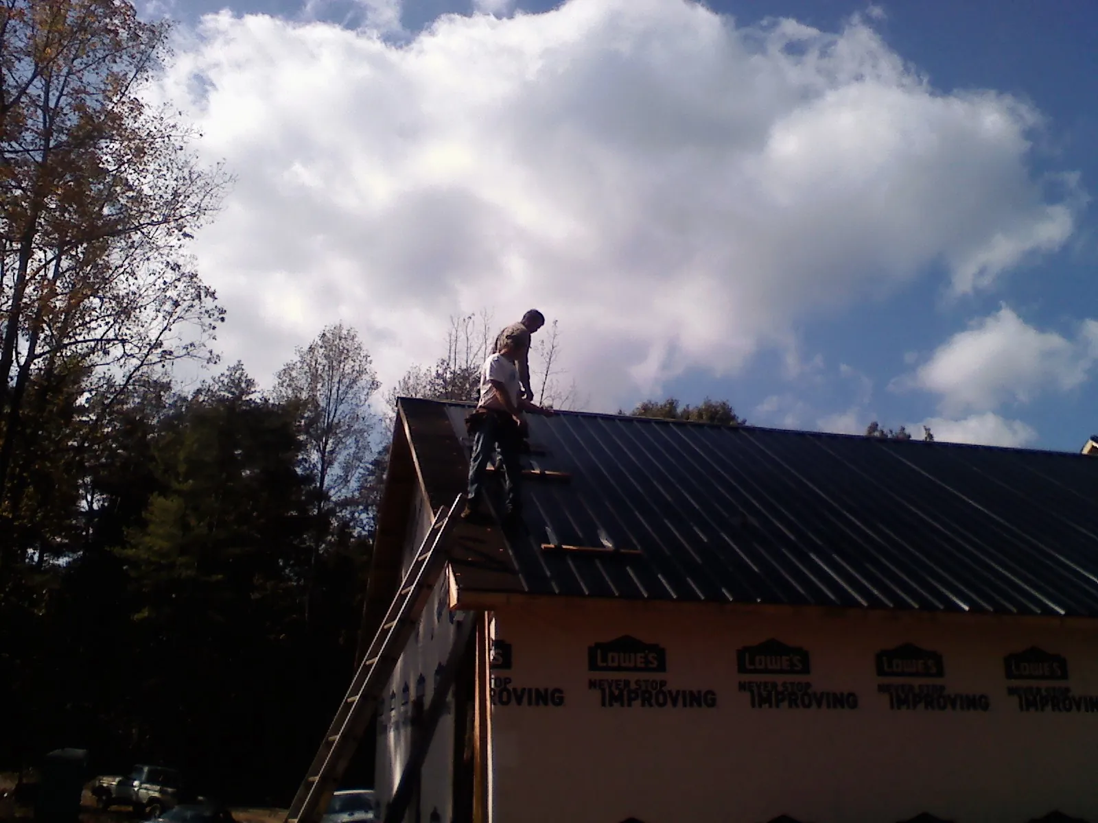 Roofer fastening dark metal panels high against a cloudy sky, from a Roof Inspection job in Hillister