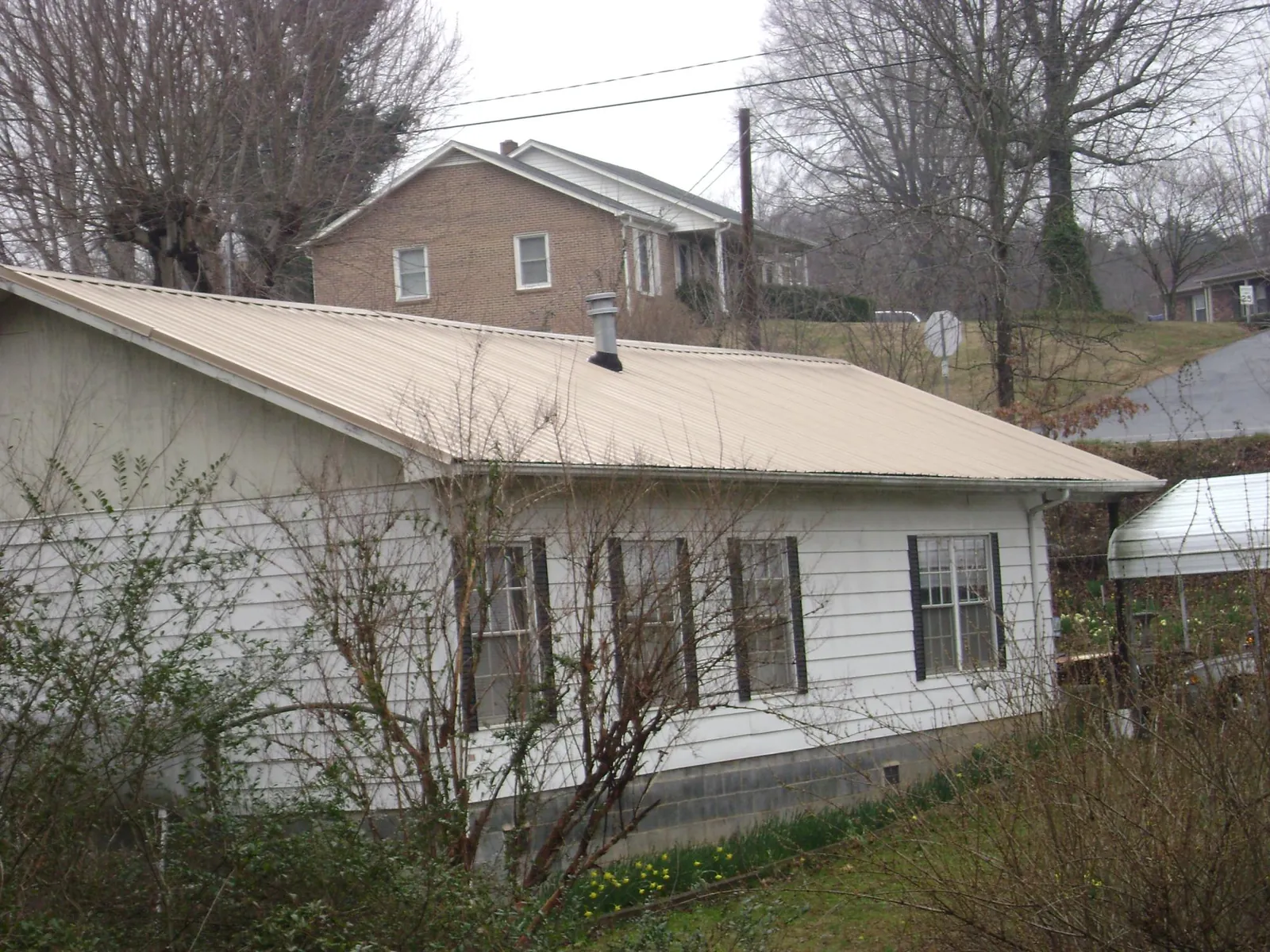 Tan metal roof on a white sided house set into a hillside — Commercial Roofing by Roofing Brothers in Hillister